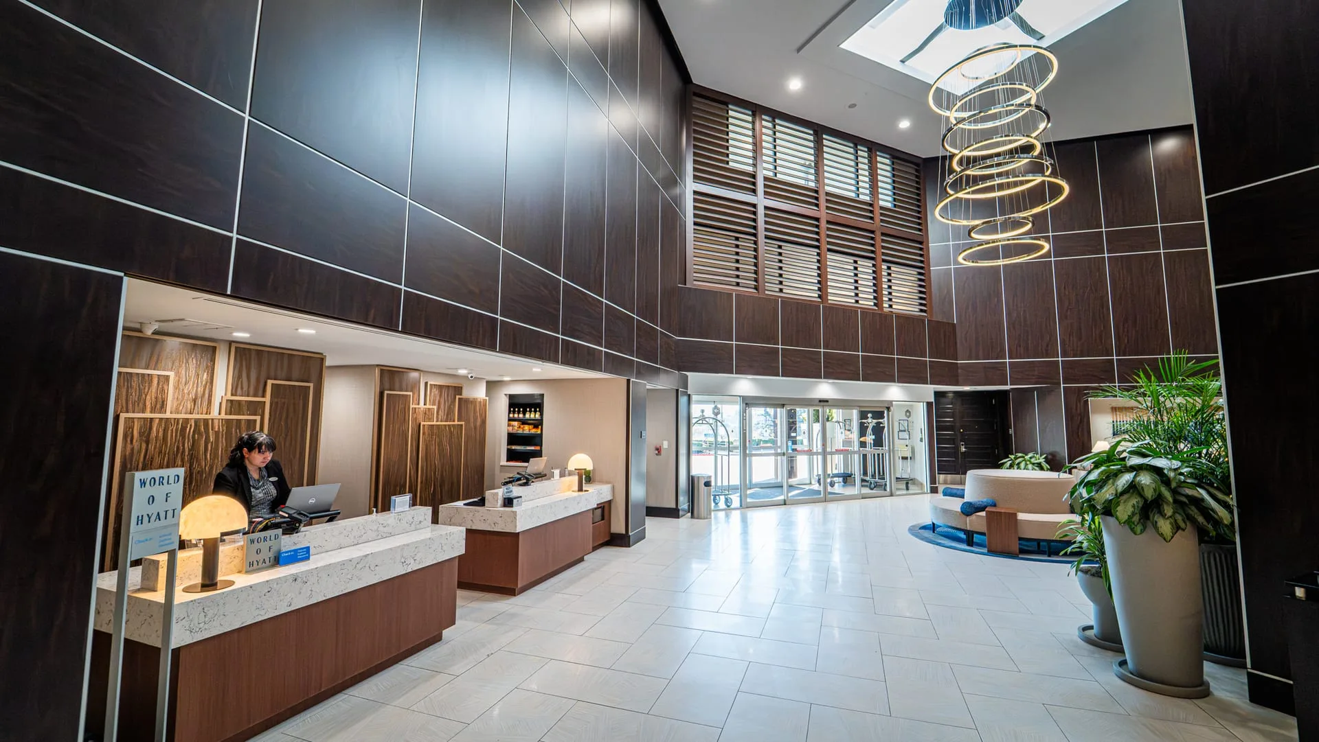 Hotel reception desks with light countertops, wood fronts and paneled back walls beneath a tall atrium