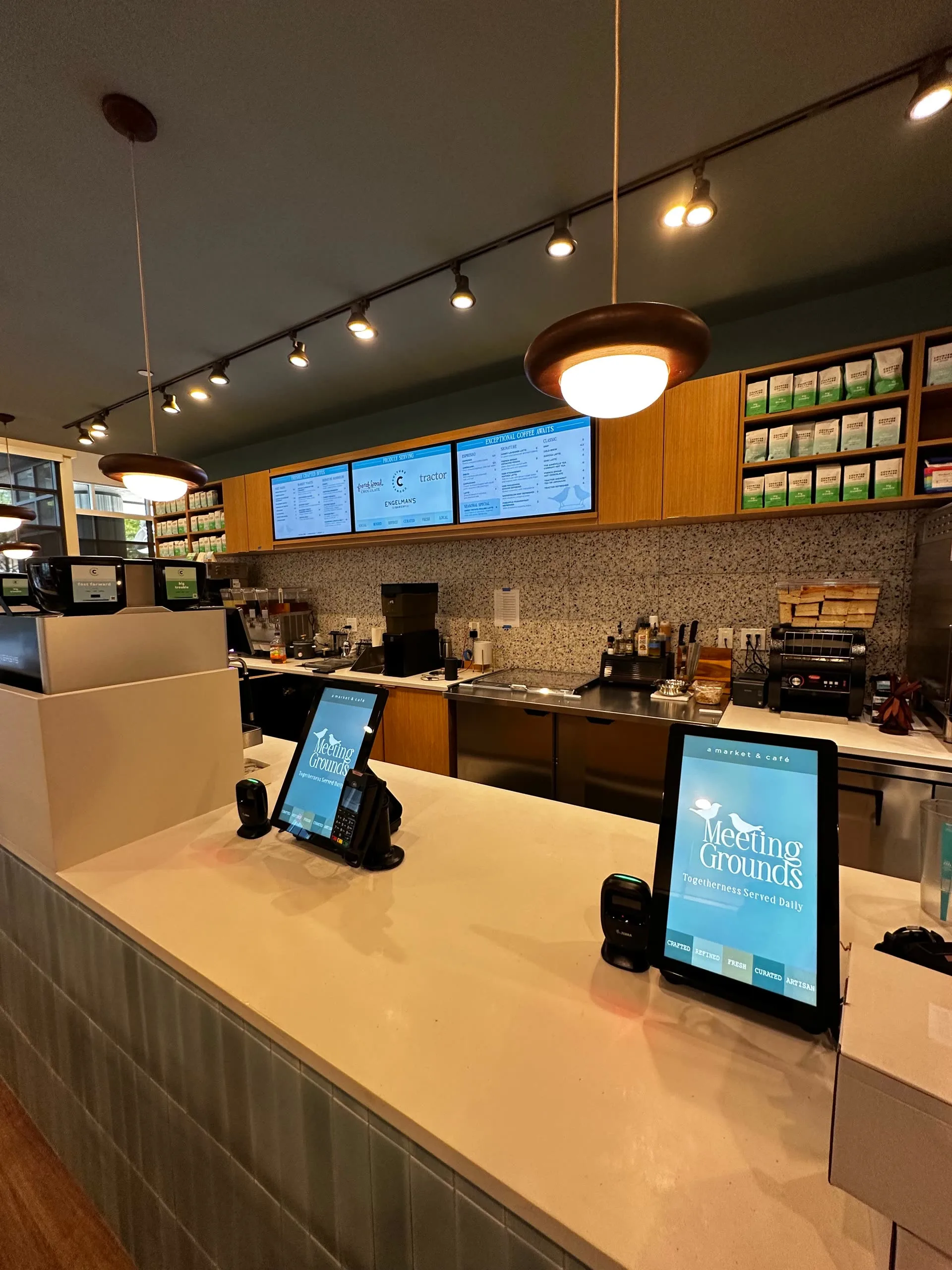 Light service countertop with ordering tablets, blue tile facing and wood-front shelving behind